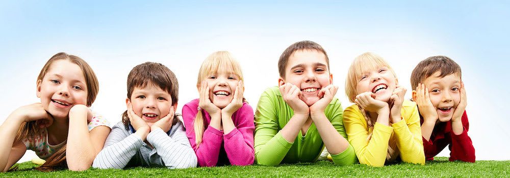 Smiling kids lying in a row on the grass